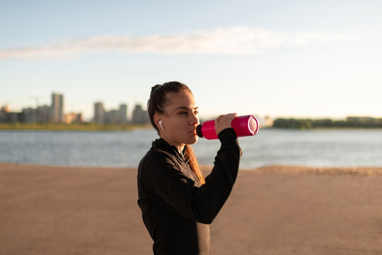 Woman in headphones drinking water on beach