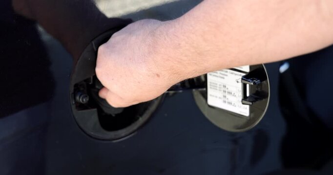 Horizontal close up perspective of a hand securely shutting the fuel door flap on a modern automobile at a gas station.