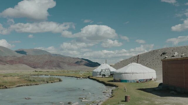 Handheld view of traditional Mongolian gers beside a winding river on the journey toward the Altai Mountains, surrounded by the vast and rugged landscape of western Mongolia under a blue summer sky.