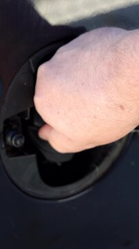 Vertical close up perspective of a hand securely shutting the fuel door flap on a modern automobile at a gas station.