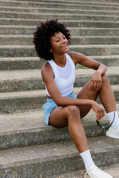 Full-body shot of a cheerful athletic woman seated on stairs