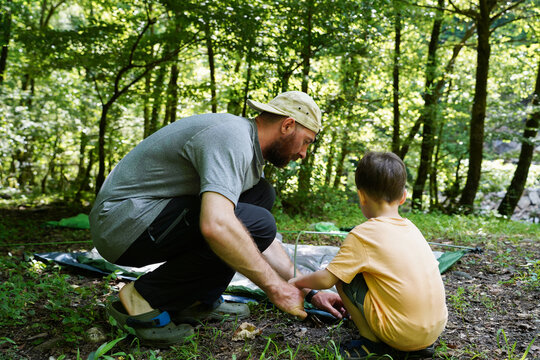 Father And Son Set Up A Tent In The Forest By The River