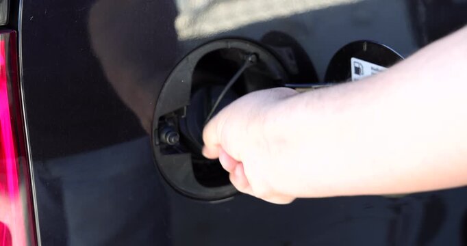 Horizontal detailed view of a person hand opening the car gas tank door compartment before refueling with petrol at a fuel pump.