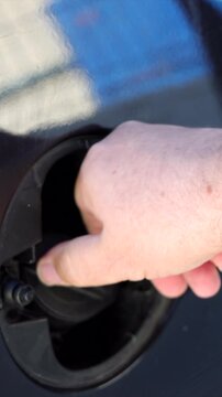 Vertical macro detail of a driver hand closing the fuel door cap on a vehicle after filling up the tank at a service station.