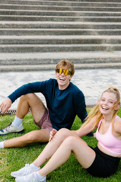 Runner couple resting on grass in a sunny park after training.