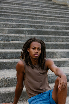 Athletic Black man with dreadlocks sitting on park stairs.