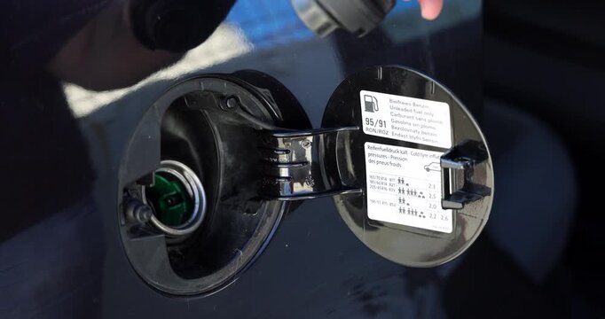 Horizontal close up view of a hand opening the exterior fuel door flap of a modern car at a gas station for refueling.