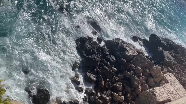 Blues waves crash against the rocks, creating a vivid and energetic coastal scene. The bright sky and deep blue sea blend beautifully of the Mediterranean Sea near Nice, Cote d'Azur, southern France
