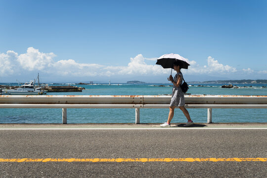 Woman Walking With Parasol Along Coastal Road