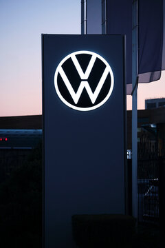 Kazakhstan, Kostanay, September 10, 2026. Glowing Volkswagen logo on tall sign at dusk with flags in background.