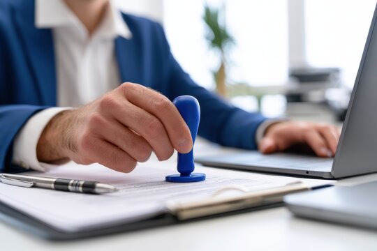 A businessman in a suit stamping a legal document at a desk with a laptop. This photo is ideal for business agreements and corporate notary concepts.