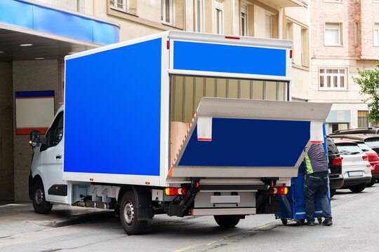 Electric delivery truck with its hydraulic tail lift lowered as a worker prepares cargo on a city street