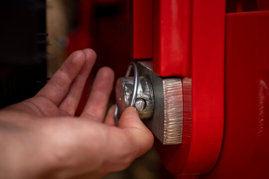 Hand inserting steel lynch pin locking fastener into metal pivot pin on red agricultural equipment mechanism.