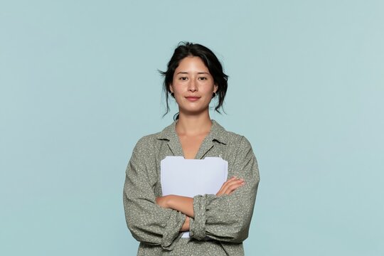 Confident Southeast Asian woman holding blank folders with folded arms, featuring a smooth skin texture and soft lighting for professional profiles and recruitment