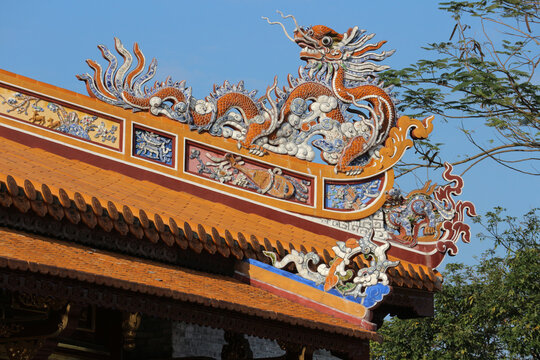 Traditional orange imperial dragon mosaic sculpture on curved roof corner, ancient pagoda rooftop clay tile architecture design