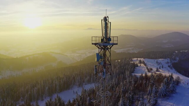 Flying over radio communications tower, mountain snow covered winter landscape.