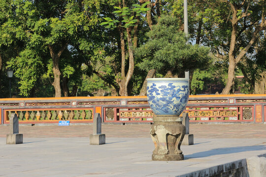 Traditional blue and white porcelain pot with dragon painting, oriental bonsai tree on carved stone pedestal at imperial palace courtyard