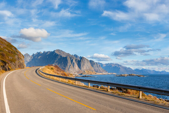 An empty asphalt road winding along a rocky sea coast with mountains under a blue sky