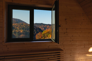 Obraz premium An open window in a wooden cabin looking out at colorful autumn forest