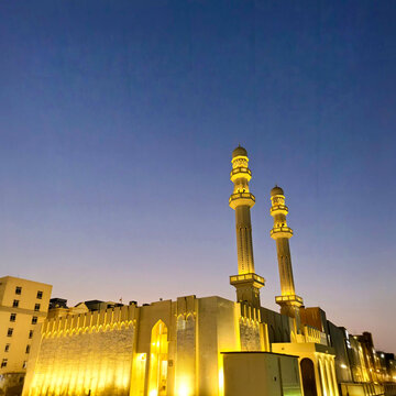 Illuminated mosque with twin minarets at dusk in Manama Bahrain featuring modern Islamic architecture geometric wall lattice and golden lighting under twilight sky