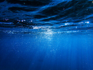 Obraz premium Underwater background with water bubbles and undersea light rays shine. Dark blue ocean surface seen from underwater. Sunbeams and Sea deep or ocean underwater a Abstract background. sunlight Nature.