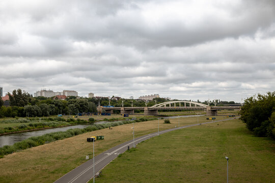 Poznan, Poland - July 8, 2026: White steel arches of Saint Roch Bridge span the Warta River, partially framed by trees along the riverfront.