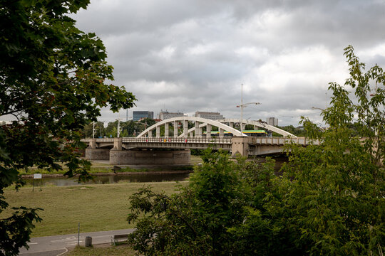 Poznan, Poland - July 8, 2026: White steel arches of Saint Roch Bridge span the Warta River, partially framed by trees along the riverfront.