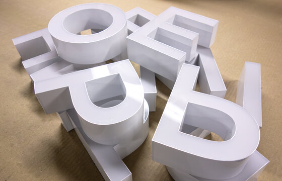 White 3D letters scattered on wooden surface. Pile of plastic alphabet characters for sign making. Typography and advertising lettering production concept.