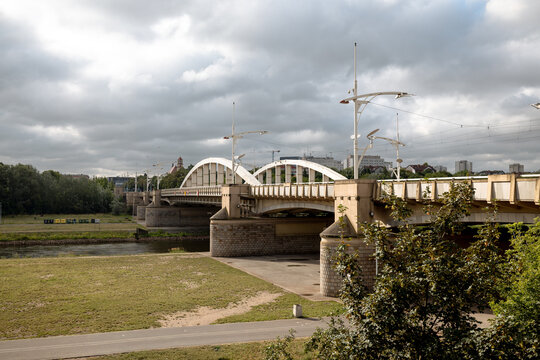 Poznan, Poland - July 8, 2026: White steel arches of Saint Roch Bridge span the Warta River, partially framed by trees along the riverfront.