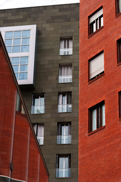 Modern residential and office buildings featuring red brick facade and dark tiled wall with geometric windows.