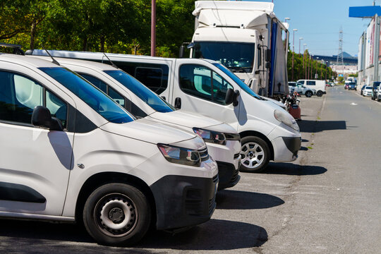A row of white commercial delivery vans and trucks parked along an industrial street