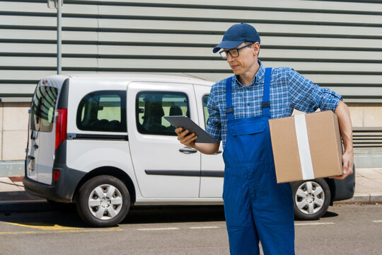 A courier holding a cardboard box and digital tablet with a delivery van in the background.