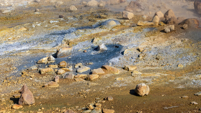 A steaming mud pool surrounded by mineral-crusted rocks and pale sulfur deposits near Kerlingarfjoll, Icelandic highlands.