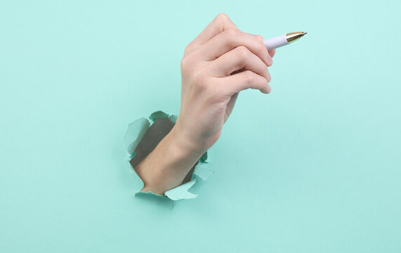 Hand holds pen through torn hole of blue paper