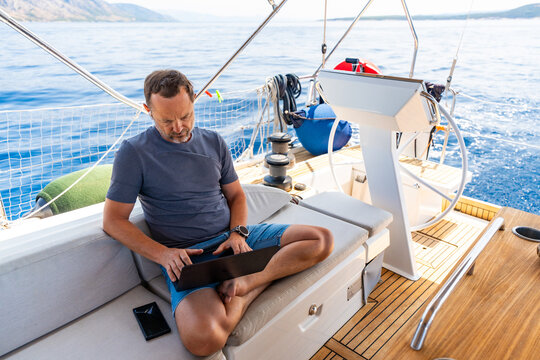 Focused man working on laptop aboard a sailing yacht. Productive remote office in a unique travel environment.