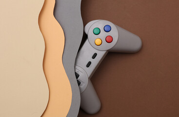 Vintage gamepad from 80s on cut paper background of wavy layers. Retro wave. Creative layout. Minimalism © splitov27