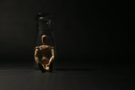 Wooden mannequin trapped sitting inside a glass jar on dark black background, concept of isolation, quarantine, depression, confinement, or feeling stuck. (161 karakter)2. 49 Kata Kunci Komersial (Bah
