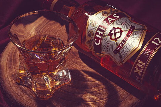 a glass of whiskey on a wooden board, next to it lies a bottle of whiskey, Chivas Regal, there are no people