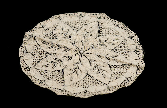 Knitted lace napkin, round crochet beige doily lace isolated on black background, crocheted Grandma's doily, detail of handmade embroidery, tablecloth, napkin, vintage art design. Craft, linen, cutout