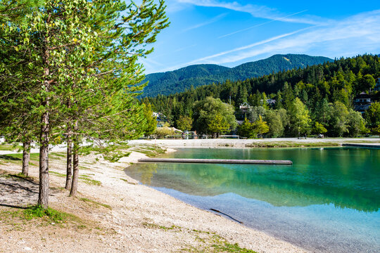 Sandy beach and pine trees on the shore of turquoise Lake Jasna with wooden pier, Kranjska Gora, Slovenia