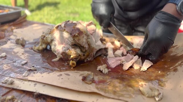 Close-up video footage of a chef wearing black gloves using a sharp knife to slice freshly smoked barbecue meat on butcher paper.
