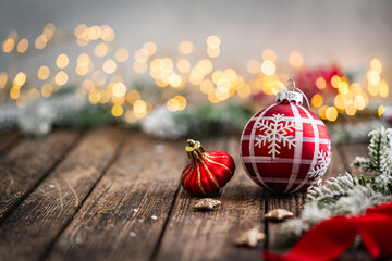 Naklejka premium A Christmas background featuring red baubles with golden glitter stripes, a star ornament, and frosted pine on a wide rustic wood table, warmly lit with twinkling lights and copy space.
