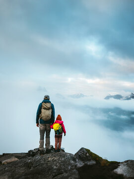 Family father and child hiking in foggy mountains with backpacks gear, active vacations in Norway parent and daughter explore Senja outdoors adventure trip together cold autumn season
