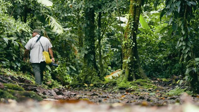 Mature latino tourist with a camera and a backpack hiking on a trail through the lush rainforest of Arenal Volcano National Park