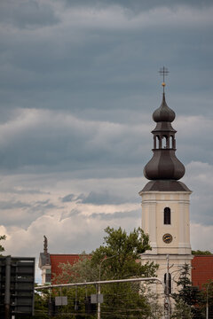 Wroclaw, Poland - July 10, 2026: White historic church tower with an onion-shaped dome and cross rises above trees beneath a cloudy morning sky.