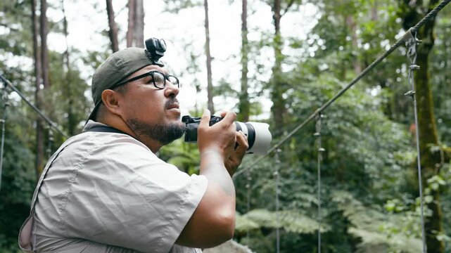 Enthusiastic male photographer capturing wildlife and landscapes with his camera on a suspension bridge in the Costa Rican rainforest