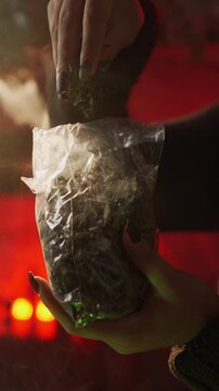 A witch brews a potion in a cauldron amidst dried herbs in an authentic home setting. She casts a spell and recites an incantation. Close-up: a hand takes dried herbs from a bag
