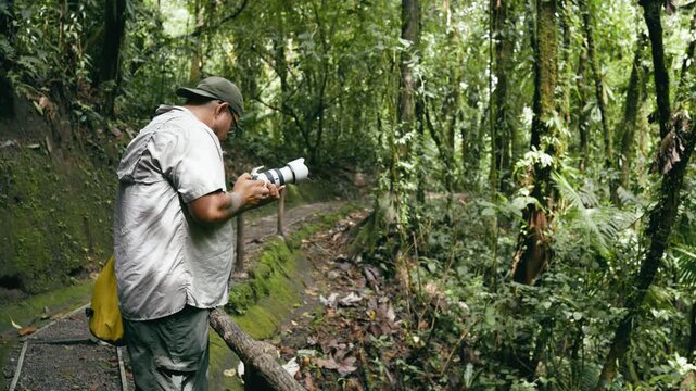 Man with a professional camera capturing images of wildlife and flora along a hiking trail. His work takes him into the heart of a dense jungle