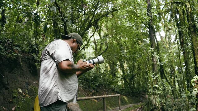 Latino wildlife photographer adjusting his professional camera with a telephoto lens inside the lush green rainforest of Costa Rica