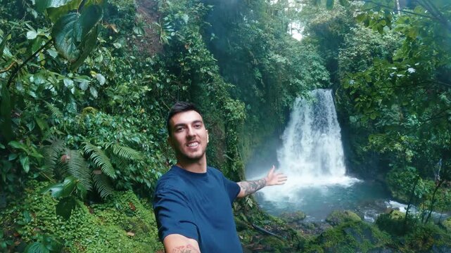 Young content creator filming himself while showing a beautiful waterfall hidden in the lush jungle of Arenal Volcano National Park